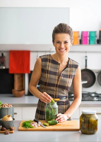 Portrait of happy young housewife pickling cucumbers in kitchen — Stock Photo, Image