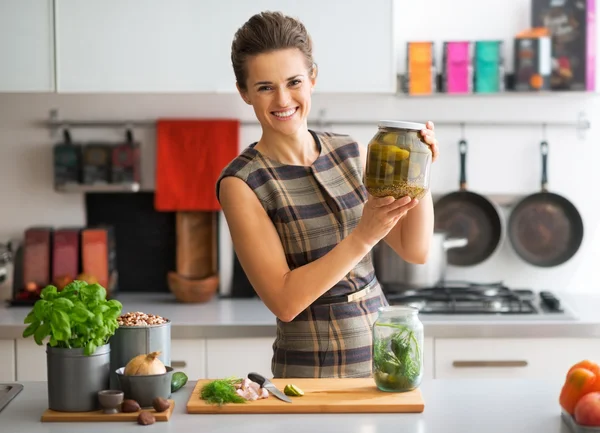 Portrait of happy young housewife showing jar of pickled cucumbe — Stock Photo, Image
