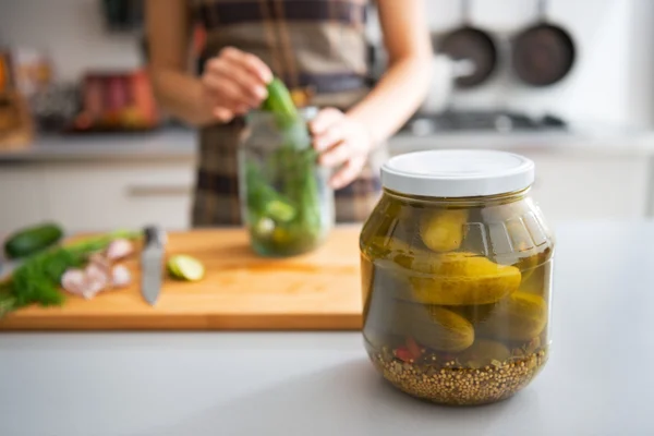 Closeup on jar of marinated cucumbers on table and housewife pic — Stock Photo, Image