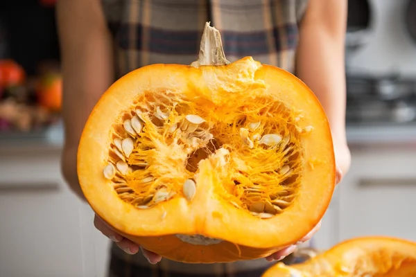 Gros plan sur la jeune femme au foyer dans la cuisine montrant la moitié de citrouille — Photo