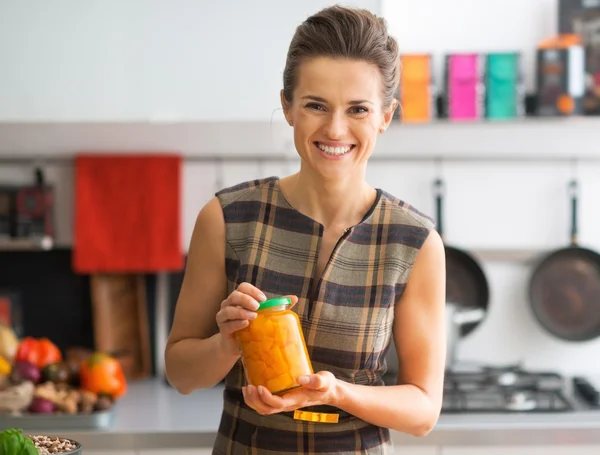 Portrait of happy young housewife showing jar of pickled pumpkin — Stock Photo, Image