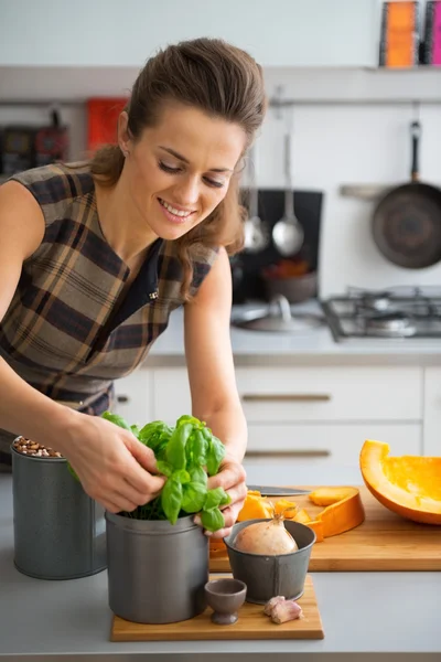Happy young housewife using fresh basil while cooking in kitchen — Stock Photo, Image