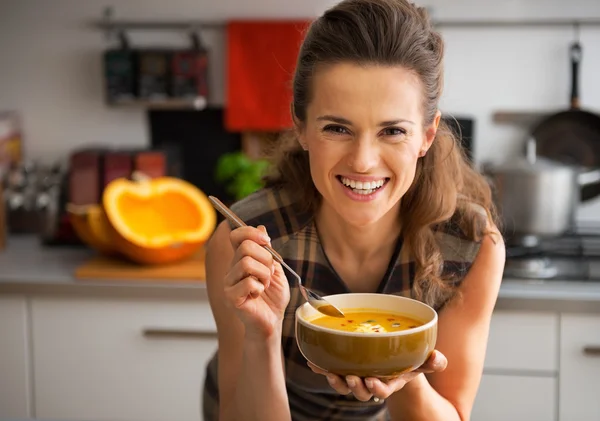 Happy young woman eating pumpkin soup in kitchen — Stock Photo, Image