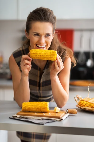 Jovem dona de casa comer milho cozido na cozinha — Fotografia de Stock