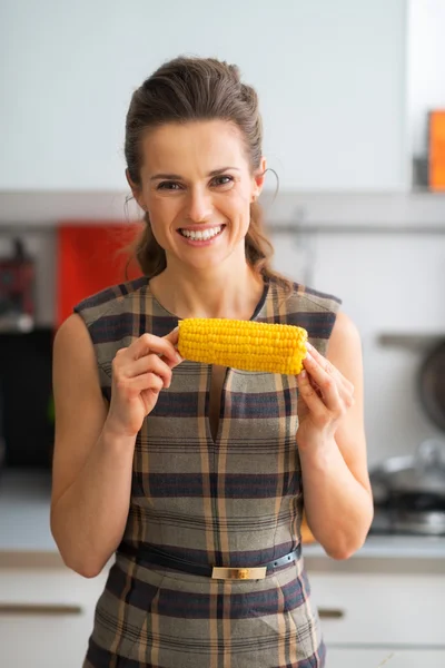 Retrato de feliz ama de casa joven comiendo maíz hervido en la cocina — Foto de Stock