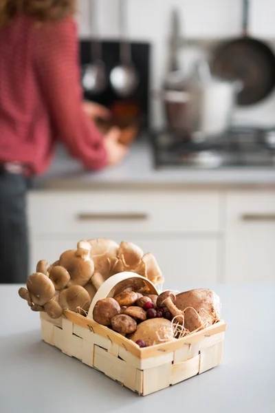 Closeup on basket with mushrooms on table and young housewife in — Stock Photo, Image