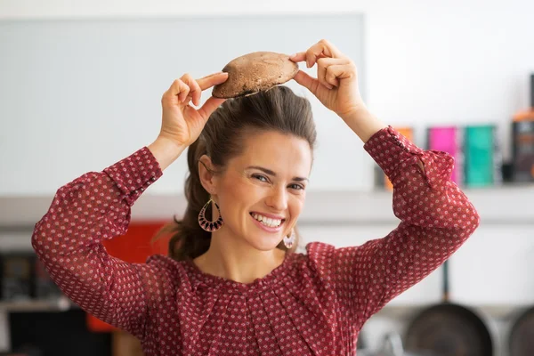 Portrait of happy young housewife using mushroom as hat — Stock Photo, Image