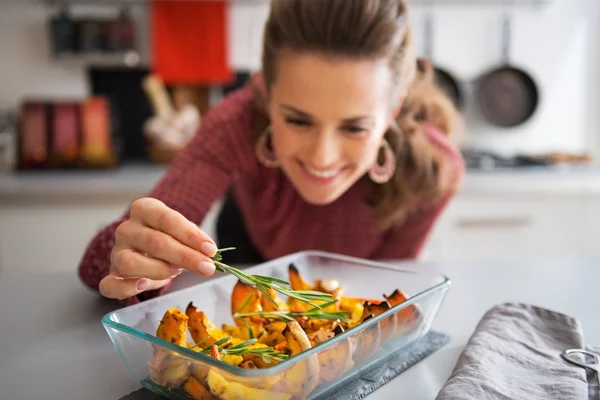 Nahaufnahme einer jungen Hausfrau, die Rosmarinus zu gebackenem Kürbis hinzufügt — Stockfoto