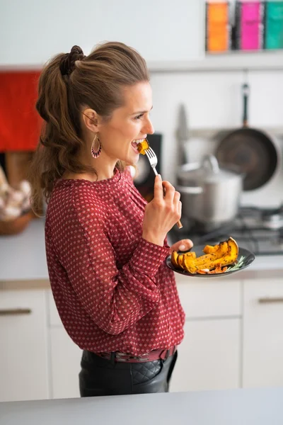 Młoda kobieta jedzenie pieczone dyni w kuchni — Zdjęcie stockowe