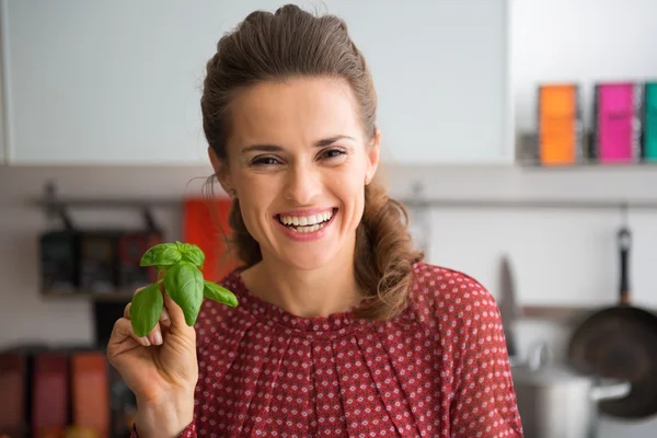 Retrato de feliz jovem dona de casa mostrando manjericão fresco — Fotografia de Stock