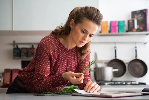 Jonge huisvrouw studeren verse kruiden kruiden in keuken — Stockfoto