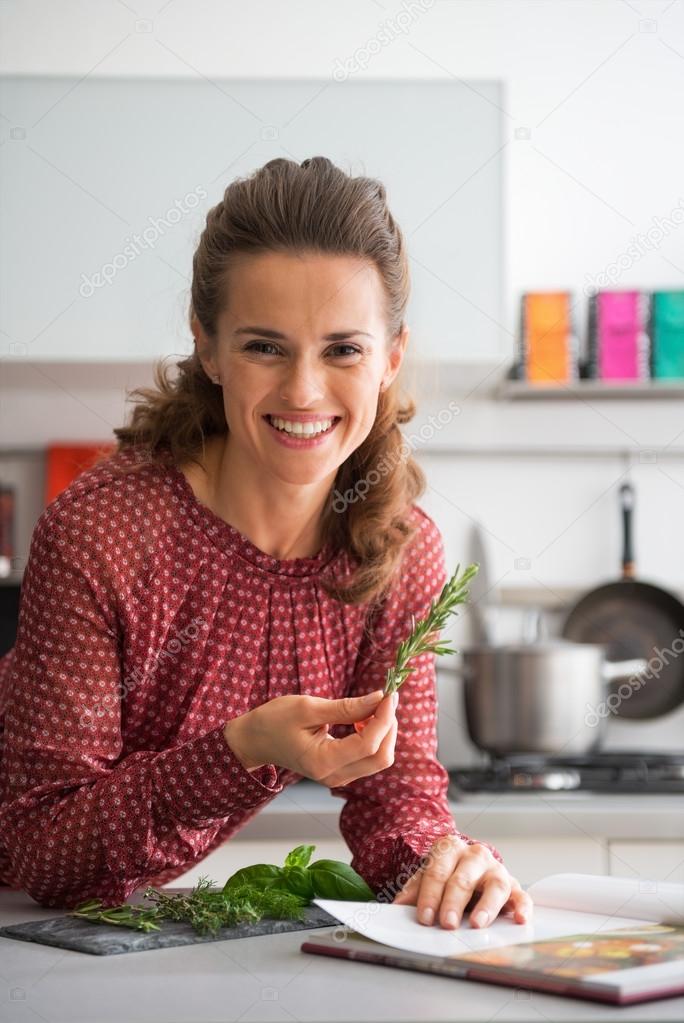 Smiling young housewife studying fresh spices herbs in kitchen