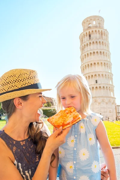 Happy mother and baby girl eating pizza in front of leaning towe