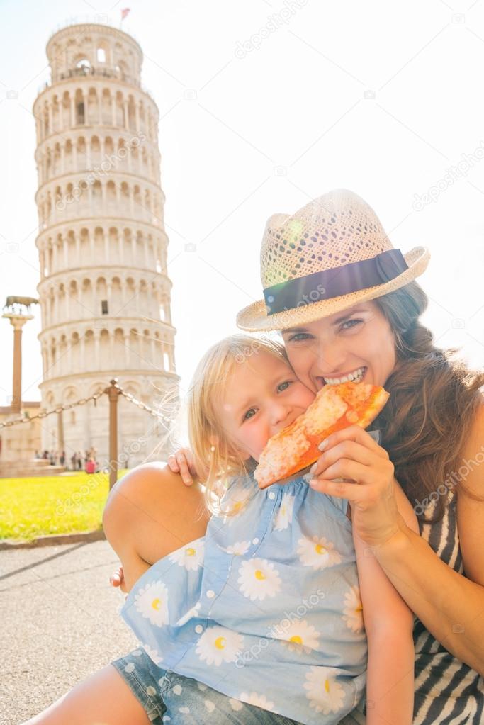 Happy mother and baby girl eating pizza in front of leaning towe