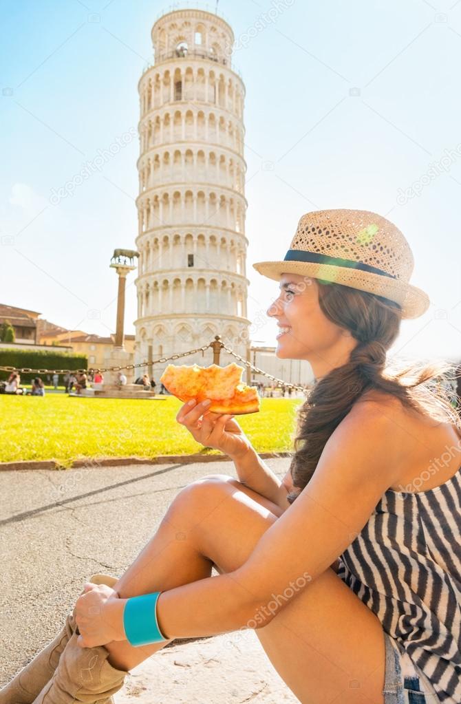 Happy young woman eating pizza in front of leaning tower of pisa