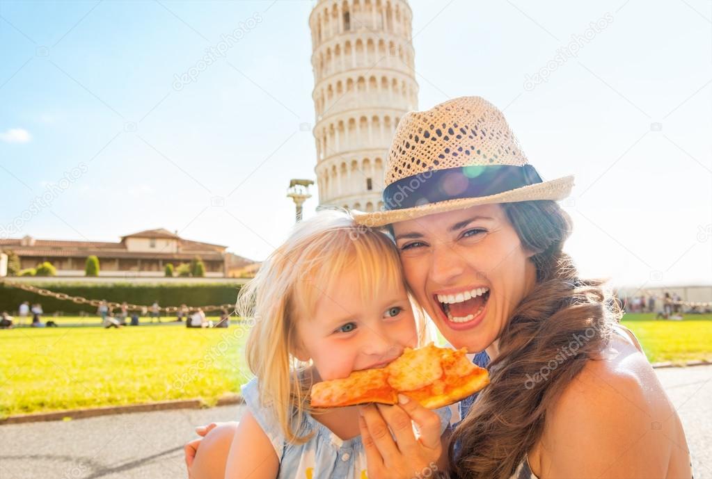 Portrait of happy mother and baby girl eating pizza in front of