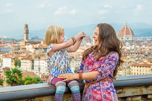 Happy baby girl taking photo of mother against panoramic view of florence, italy — 图库照片