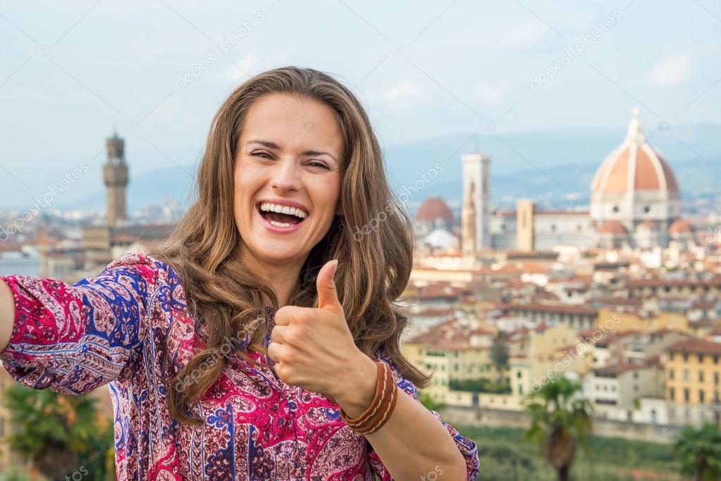 Happy young woman making selfie and showing thumbs up against panoramic view of florence, italy