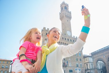 Happy mother and baby girl making selfie in front of palazzo vec clipart