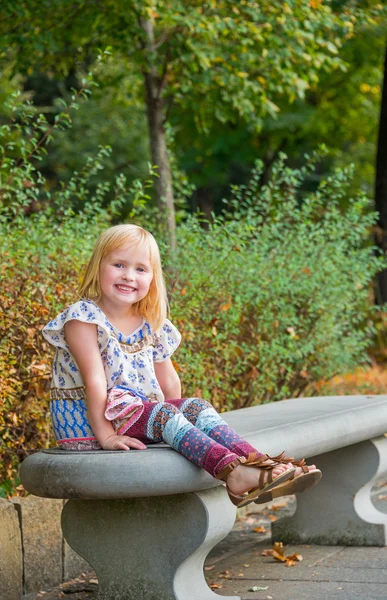 Portret van lachende meisje, zittend op de Bank in stadspark — Stockfoto