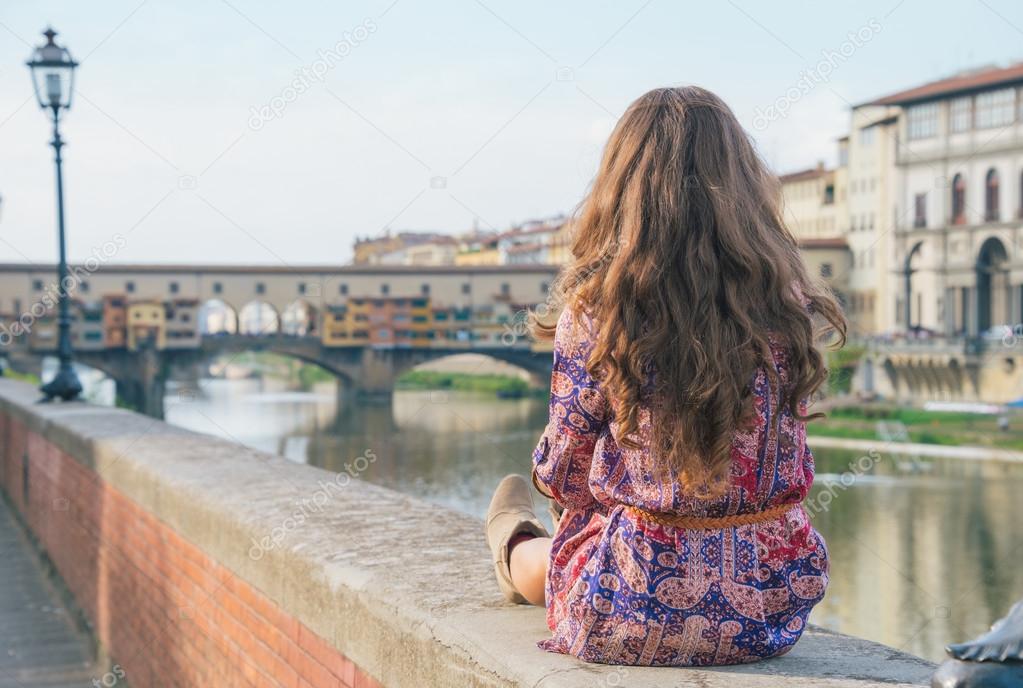 Young woman sitting near ponte vecchio in florence, italy. rear 