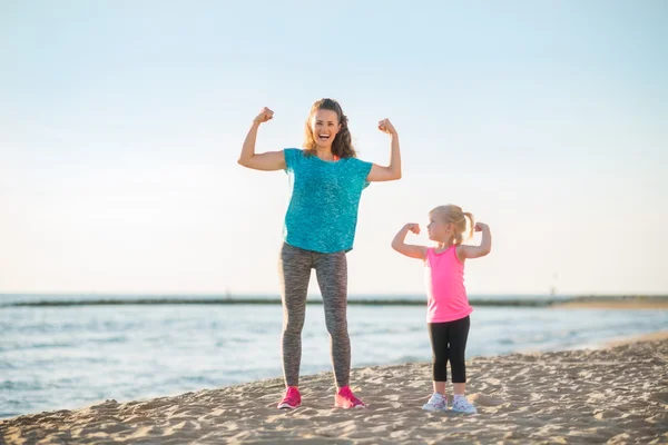 Healthy mother and baby girl showing biceps on beach — Stock Photo, Image