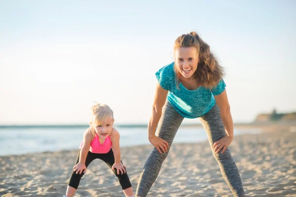 Zdravá matka a dítě dívka cvičení na pláži ve večerních hodinách — Stock fotografie