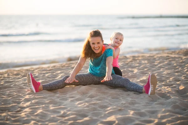 Healthy mother and baby girl stretching on beach in the evening — Stock Photo, Image