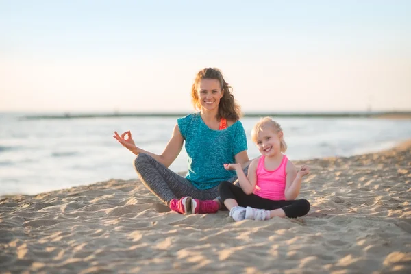 Healthy mother and baby girl doing yoga on beach in the evening — Stock Photo, Image