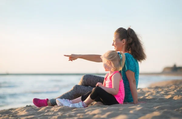 Córeczkę i matkę wskazując siedząc na plaży w nawet — Zdjęcie stockowe
