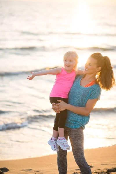 Mère saine et bébé fille pointant tandis que sur la plage dans le pair — Photo