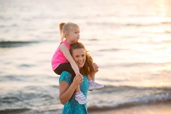 Happy baby girl sitting on shoulders of mother on beach in the e — Stock Photo, Image