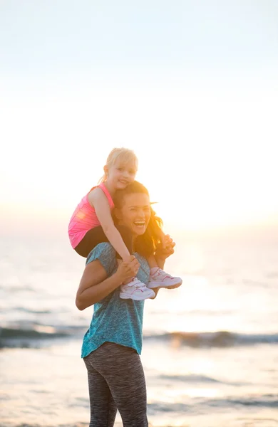 Glücklich Baby Mädchen sitzt auf den Schultern der Mutter am Strand in der e — Stockfoto