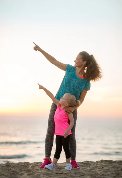 Healthy mother and baby girl on beach in the evening pointing — Stock Photo, Image