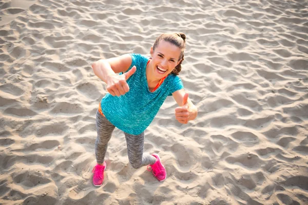 Happy fitness young woman on beach showing thumbs up — Stock Photo, Image