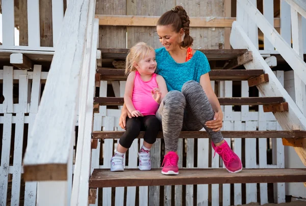 Healthy mother and baby girl sitting on stairs of beach house — Stock Photo, Image