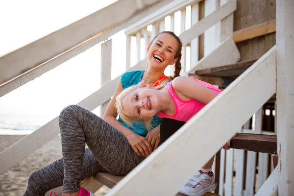 Healthy mother and baby girl sitting on stairs of beach house — Stock Photo, Image