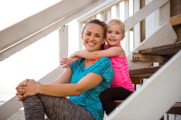 Healthy mother and baby girl hugging on stairs of beach house — Stock Photo, Image