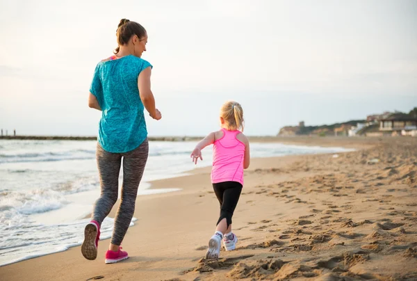 Frisk mamma och baby flicka kör på stranden. bakifrån — Stockfoto