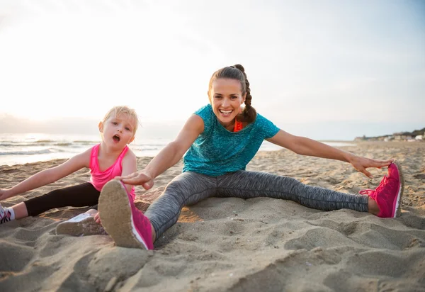 Gesunde Mutter und Mädchen dehnen sich am Abend am Strand — Stockfoto