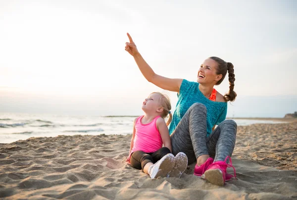 Gesunde Mutter und kleines Mädchen, die abends am Strand sitzen und — Stockfoto