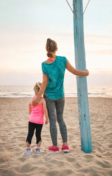 Healthy mother and baby girl on beach in the evening looking int — Stock Photo, Image