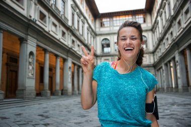 Happy fitness woman showing victory gesture near uffizi gallery  clipart