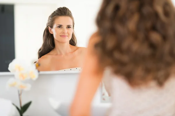Happy young woman looking in mirror in bathroom — Stock Photo, Image