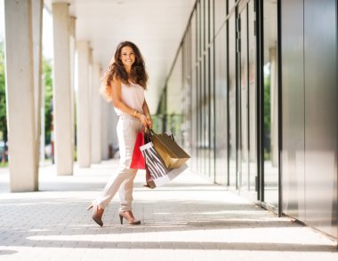 Renkli alışveriş torbaları ile poz gülümseyen, kahverengi saçlı kadın