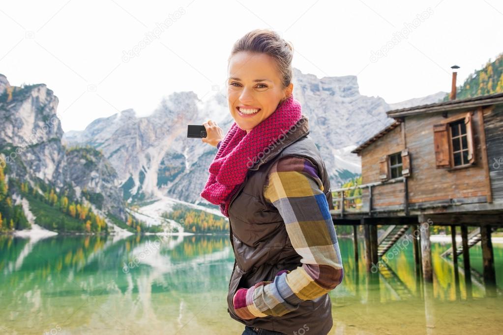 Smiling woman at Lake Bries aiming digital camera at Dolomites