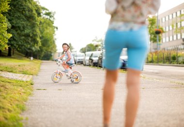 Anne izliyor gibi gülümseyen kız şehir kaldırımda bisiklet sürmek