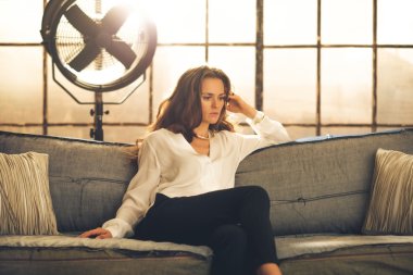 Elegant woman sitting on a sofa, crossing legs, in a loft clipart