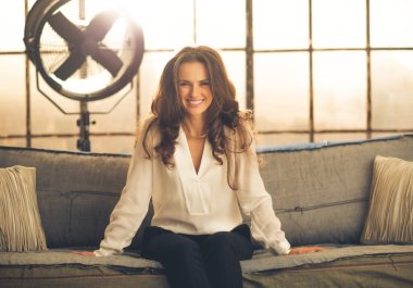 Gülümseyen, zarif kadın kanepe çatı katında oturan ileriye doğru eğilerek