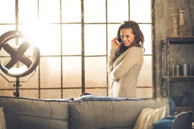 Kanepenin arkasında telefonda konuşurken çatı katında gülümseyen esmer standları